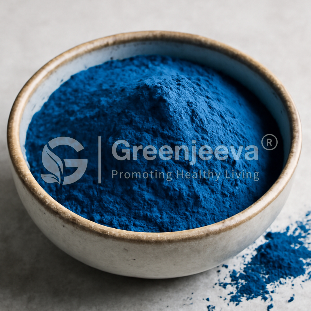 A close-up of a bowl filled with vibrant blue spirulina powder, with some powder spilled on the surface beside it.