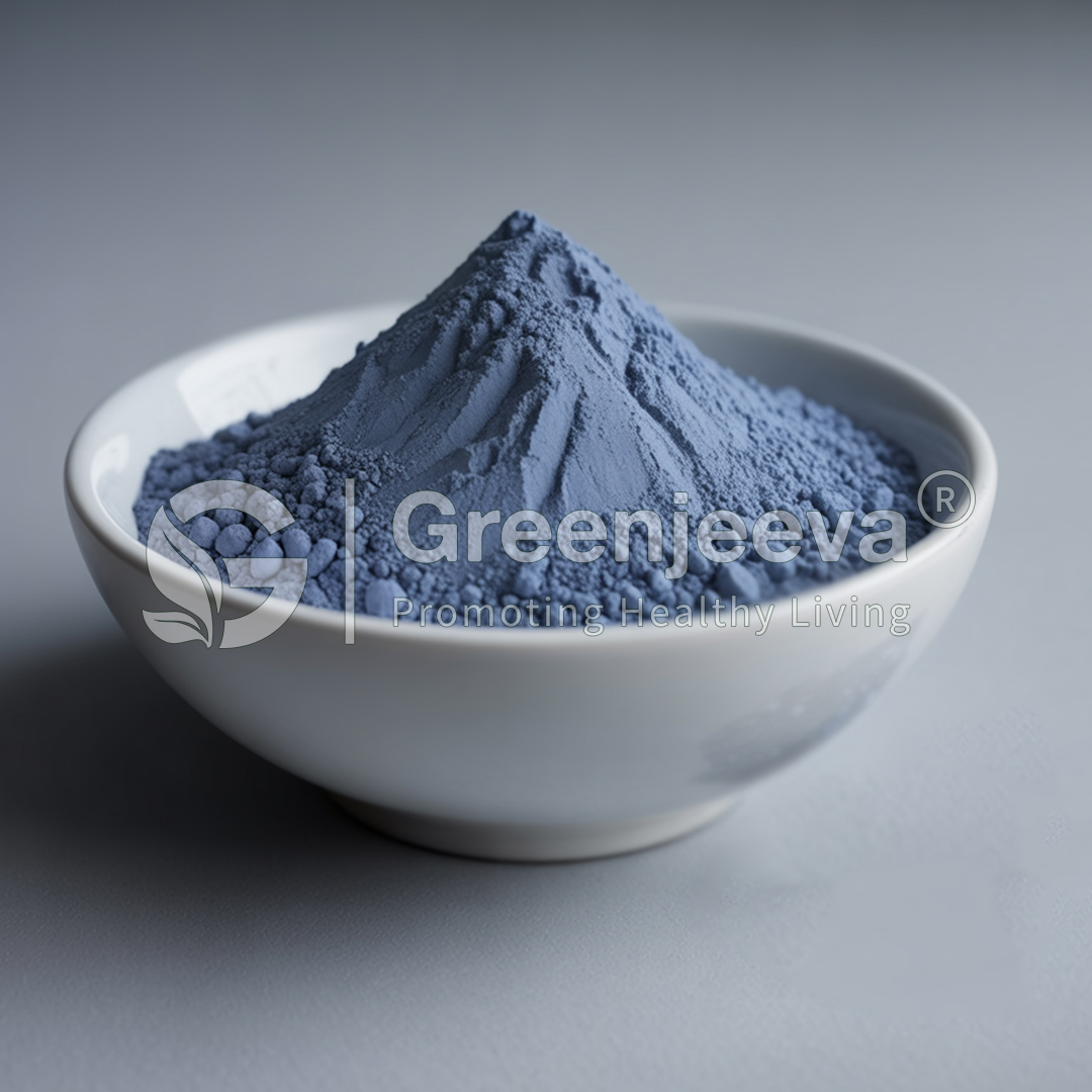 A bowl filled with blue powder, resembling a mountain, set against a smooth gray background. Greenjeeva logo visible.