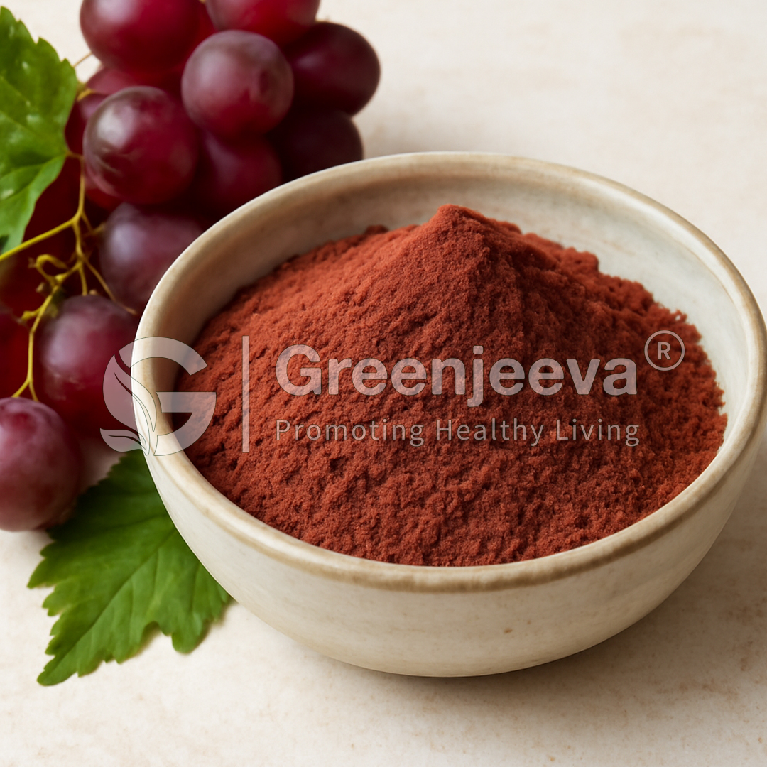 A bowl of vibrant red powder sits next to a cluster of dark grapes and green leaves, representing healthy living and nutrition.