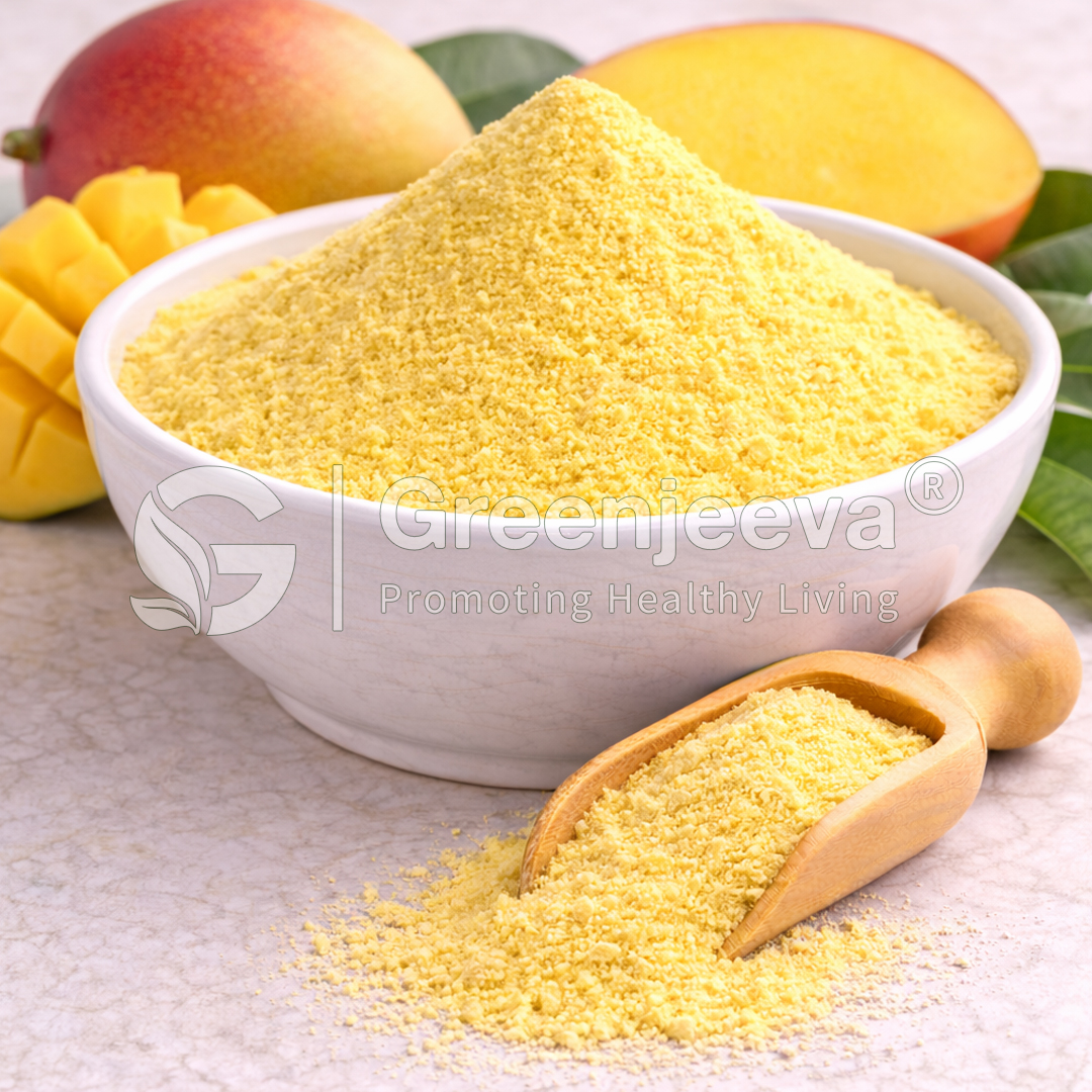 Bowl of bright yellow mango powder with a wooden scoop, surrounded by fresh mangoes and green leaves on a textured surface.